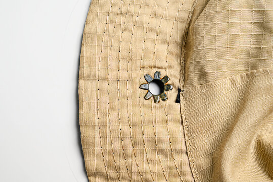 Macro shot of a tan boonie hat's brim and crown, featuring durable ripstop fabric, parallel stitching, and a star-shaped metal ventilation eyelet on a white background