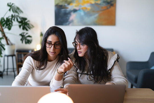 Two women collaborate on a project, looking intently at their laptops. They are engaged in discussion and problem-solving in a modern office setting.