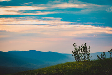 Obraz premium Sunset over layered mountain ridges in the Bieszczady Mountains, seen from Wielka Rawka and Mała Rawka viewpoints. Peaceful nature landscape with dramatic sky and soft evening light. 