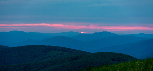 Sunset over layered mountain ridges in the Bieszczady Mountains, seen from Wielka Rawka and Mała Rawka viewpoints. Peaceful nature landscape with dramatic sky and soft evening light.
