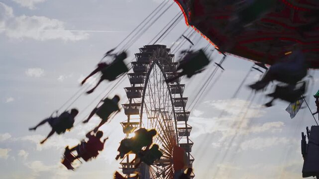 Swing ride Wellenflug and Ferris wheel Willenborgs Riesenrad at Oktoberfest in Munich, Theresienwiese. Iconic fairground attractions of Bavaria with festive atmosphere and Bavarian tradition