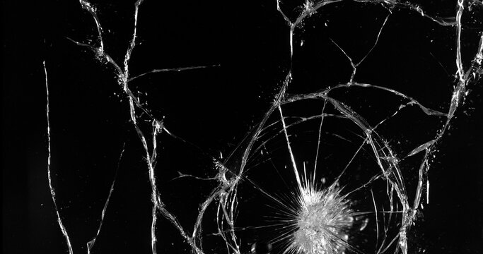 Front view photo of glass shattered by a bullet. Gunshot impact creates cracks, flying shards and dust isolated on black background. Perfect VFX overlay element or dramatic background.