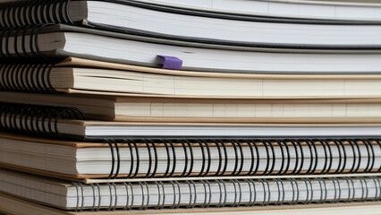 A stack of notebooks with varying sizes and page layouts, showcasing different types of paper and binding styles, viewed from a close-up perspective