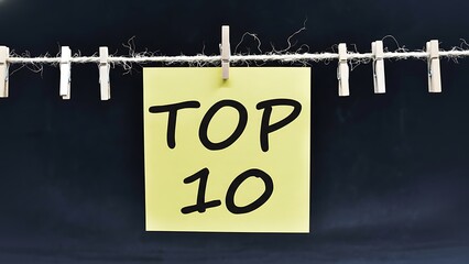 Yellow sticky note with bold black text 'TOP 10' hanging on clothesline with wooden clips against dark background