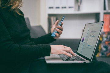 Woman makes an online payment using two-factor authentication. Girl entering a password on laptop while using a smartphone for 2fa verification. Secure online transactions and digital security.