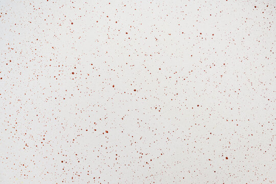 Close-up of a white surface featuring a fine pattern of reddish-brown paint splatters and spots, creating a clean abstract texture for design backgrounds