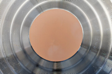 Macro shot of the bottom of a professional cookware pan showing metallic concentric ridges for even heat distribution and a central orange core. Industrial and abstract background