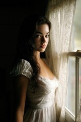 Fototapeta premium A young woman in a white dress stands by a lace-curtained window, gazing softly at the camera as light pours in. Concept Soft window-light portrait, White dress elegance, Lace-curtained backdrop