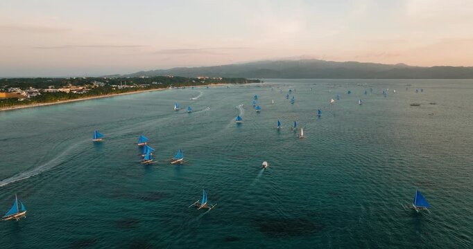 Drone view following the sunset sailboats over clear water. Boracay, Philippines.
