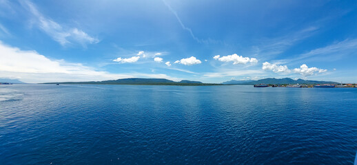 A calm sea view with mountains in the distance and blue skies.