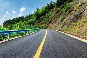 Fototapeta premium Scenic asphalt road winding through green mountains under a bright blue sky.