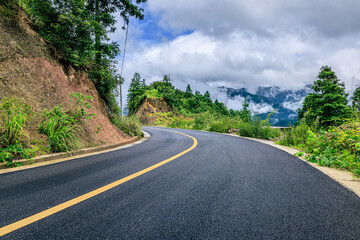 Scenic winding asphalt road through lush green mountains under a cloudy sky in the countryside.