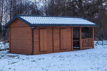 Drewniany, niewielki domek z dwuspadowym dachem pokrytym śniegiem, położony na działce rekreacyjnej zimą Konstrukcja ma pionową drewnianą elewację i zamknięte okiennice. Po prawej stronie mała weranda © Grzegorz