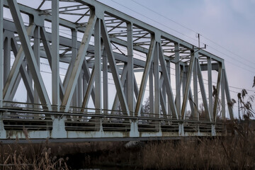Stalowy most kolejowy nad rzeką Kamienną na obrzeżach miasta – Ostrowca Świętokrzyskiego w zimowej szarości. Konstrukcja ma budowę kratownicową z dużymi stalowymi belkami tworzącymi trójkątne wzory.  © Grzegorz
