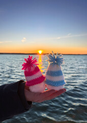 person holding cute snowman with knitted hats on the winter beach in sunset	

