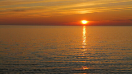 A stunning sunset over tranquil waters, reflecting shades of orange and gold. The sun dips low on the horizon, casting a warm glow across the calm sea.