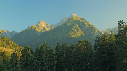 Mountain peaks and green forest landscape during golden hour sunset.