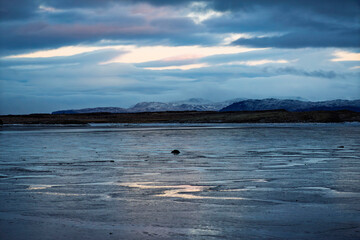 Naklejka premium Moody winter landscape of frozen coastal waters under dramatic clouds and snowy mountains at twilight