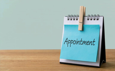 Appointment Text Written on Blue Sticky Note Attached to Desk Calendar on Wooden Table for Scheduling Concept