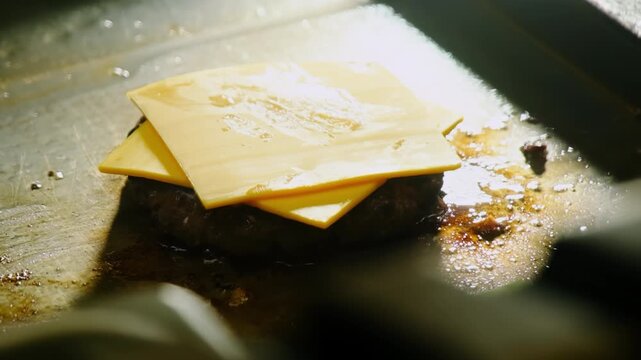 Chef hand presses cheese slices on beef cutlet on hot grill closeup. Cook master in gloves prepares fresh cheeseburger in fast food restaurant