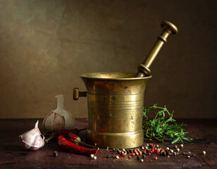 Vintage brass mortar and pestle with garlic, chili peppers, and herbs on a wooden table