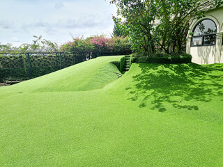 A green synthetic grass field with mounds of hills and a tree shading the green grass. Green meadow...