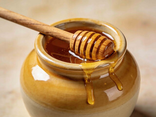 Golden honey dripping from a wooden dipper into a ceramic pot
