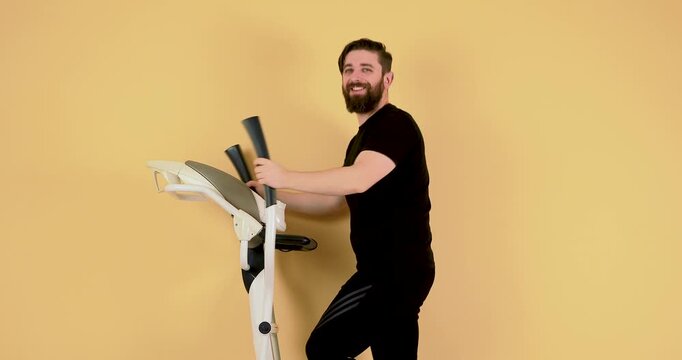 A bearded Caucasian man exercises on an elliptical trainer and gives a thumbs-up to the camera, expressing a positive &ldquo;sport is life&rdquo; mindset. This 4K video represents motivation, fitness, healthy lif