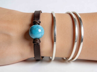 Hand wearing stacked bracelets: leather with turquoise bead and silver bangles
