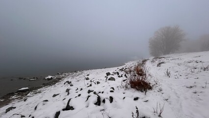 Snowy foggy river shore. Winter romantic landscape. Monochrome nature.