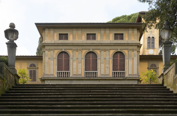 Neoclassical architectural facade with arched windows and columns, part of Villa Stibbert in Florence, Italy, seen from a stone staircase.