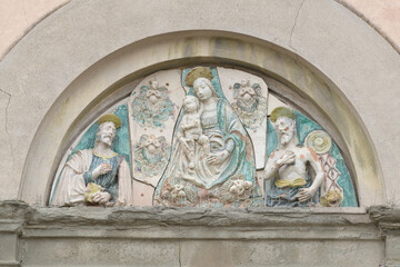 Glazed terracotta lunette with Madonna and Child between saints above the portal of San Giuseppe Church in Lucca, Italy, in Della Robbia style.