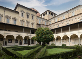 View of the cloister of the Basilica di San Lorenzo with central tree, trimmed hedges, and Renaissance arcades, Florence, Italy.