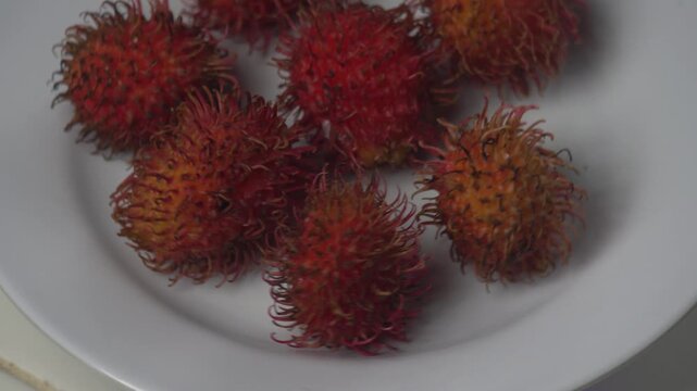 A plate of fresh, ripe red rambutan fruits (Nephelium lappaceum) featuring their unique hairy skin. This high-quality 4K footage showcases the vibrant colors of tropical exotic fruits, ideal for healt