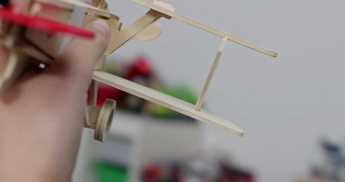 Active child hand moves small wooden airplane through open space in playroom closeup. Happy kid plays with vintage plane made of plywood constructor at home POV