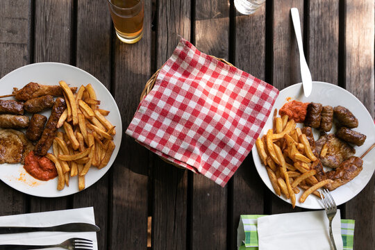 piatti su un tavolo di legno apparecchiato, con patate fritte, salsa ajvar e grigliata mista di carne, di giorno, a pranzo, in Slovenia