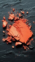 Vibrant orange eye shadow crumbles against a dark, textured backdrop. Beauty, cosmetics, and artistry merge in this abstract composition.