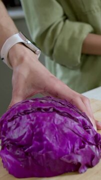 Vertical video: Reaching cook hands holding red cabbage and slicing for salad at counter with knife