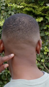 Vertical video: Leaning in, yellow friend tracing nape in garden, checking cut, crescent earring