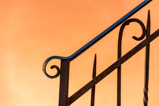 minimalist detail of a wrought iron railing with orange color background