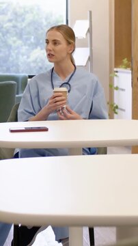 Vertical video: Colleague speaking, nurse in scrubs holding cup in lounge on break, tucking hair