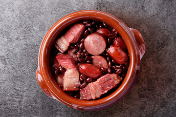 Brazilian feijoada served in a clay pot on a cement base, with black beans, sausage, bacon, and pork in a rich broth