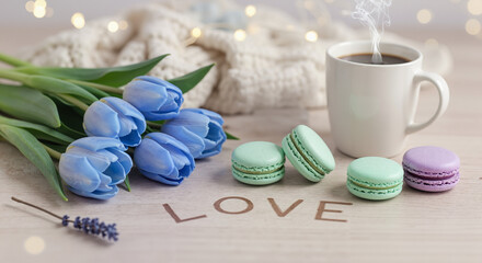 Colorful macarons with coffee and blue tulips on wooden table  