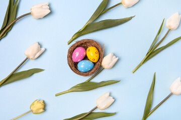 Easter colored painted eggs in bird nest with white tulips on gray background with space for text and greetings. Easter and spring concept. Spring background