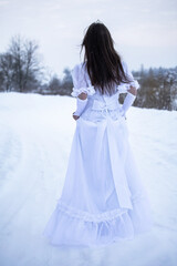 Snow Queen. A young girl in a white dress in the snow. Girl in a white dress. Bride. Winter cold weather. Model. Young woman in winter park.