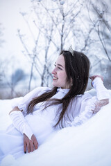 Snow Queen. A young girl in a white dress in the snow. Girl in a white dress. Bride. Winter cold weather. Model. Young woman in winter park.