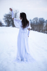 Snow Queen. A young girl in a white dress in the snow. Girl in a white dress. Bride. Winter cold weather. Model/ Young woman in winter park.