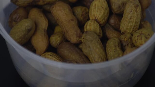 Close up of freshly boiled peanuts in their shells served in a transparent bowl. Rotating shot of healthy organic legume snacks, a popular traditional street food in Southeast Asia. Detailed texture o