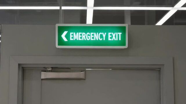Emergency exit sign with left arrow above doorway in modern office corridor