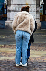 A fashionable woman wearing light blue denim jeans and a beige faux fur jacket walking outdoors during a cold winter day.